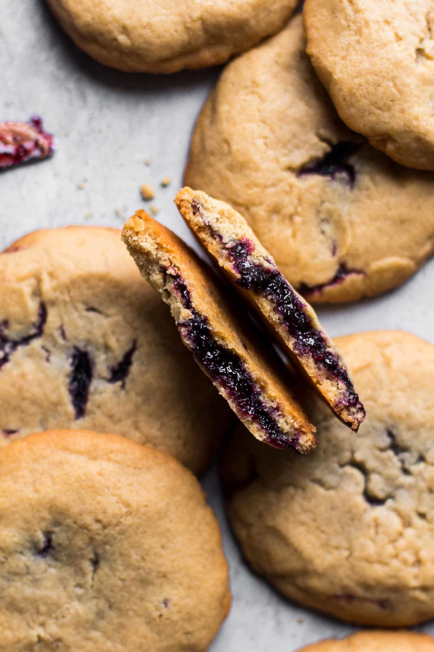 half dozen peanut butter and jelly cookies with one being broken in the center and jelly oozing out of the center