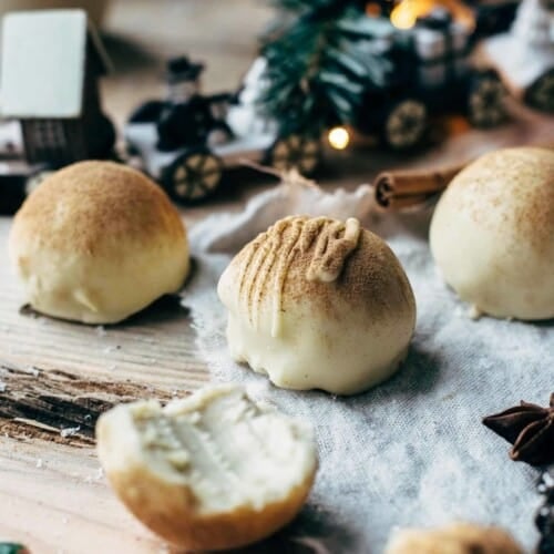 A few eggnog truffles on a wooden table with one truffle being half eaten