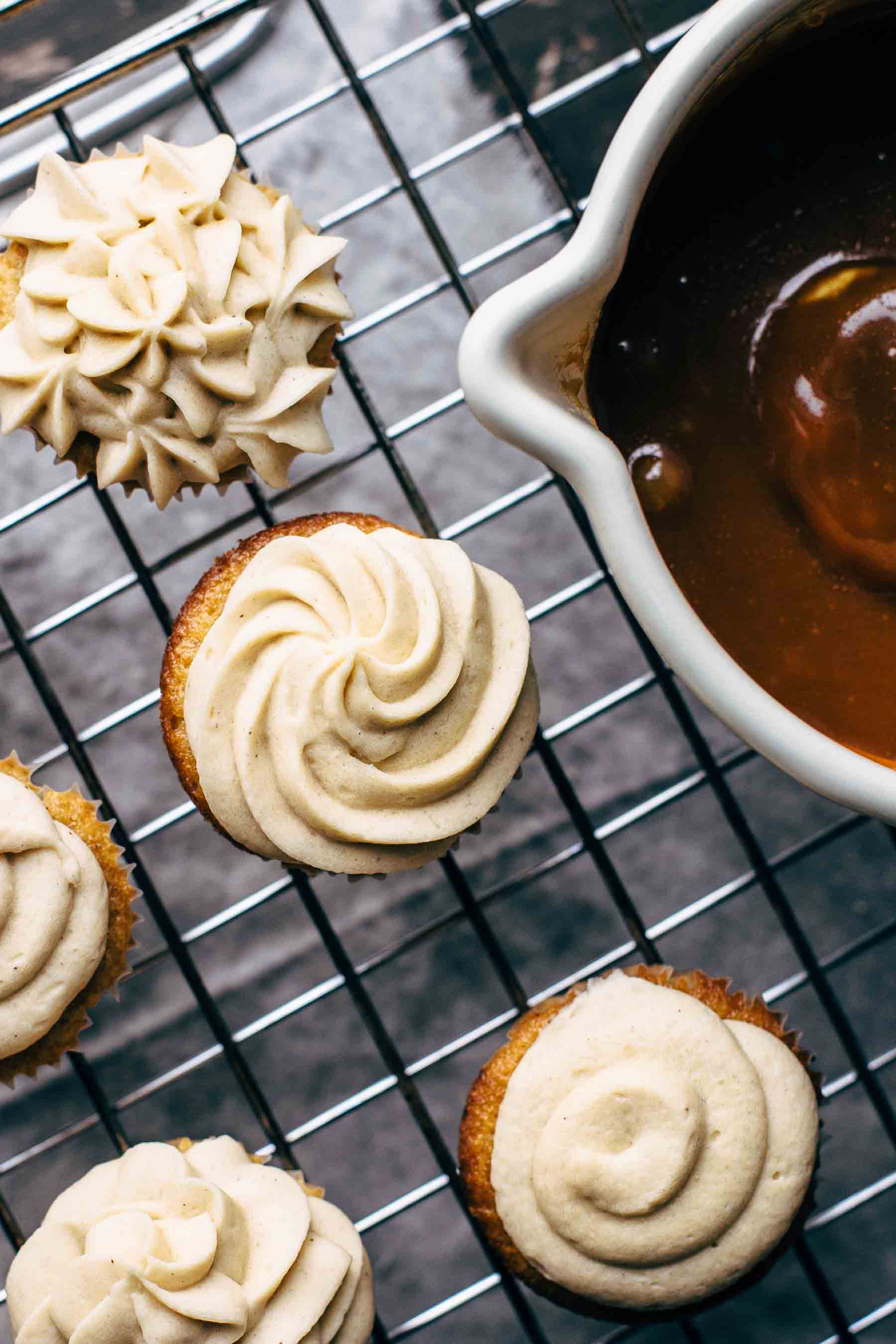 Frosted cupcakes o a wire rack with a pan full of caramel