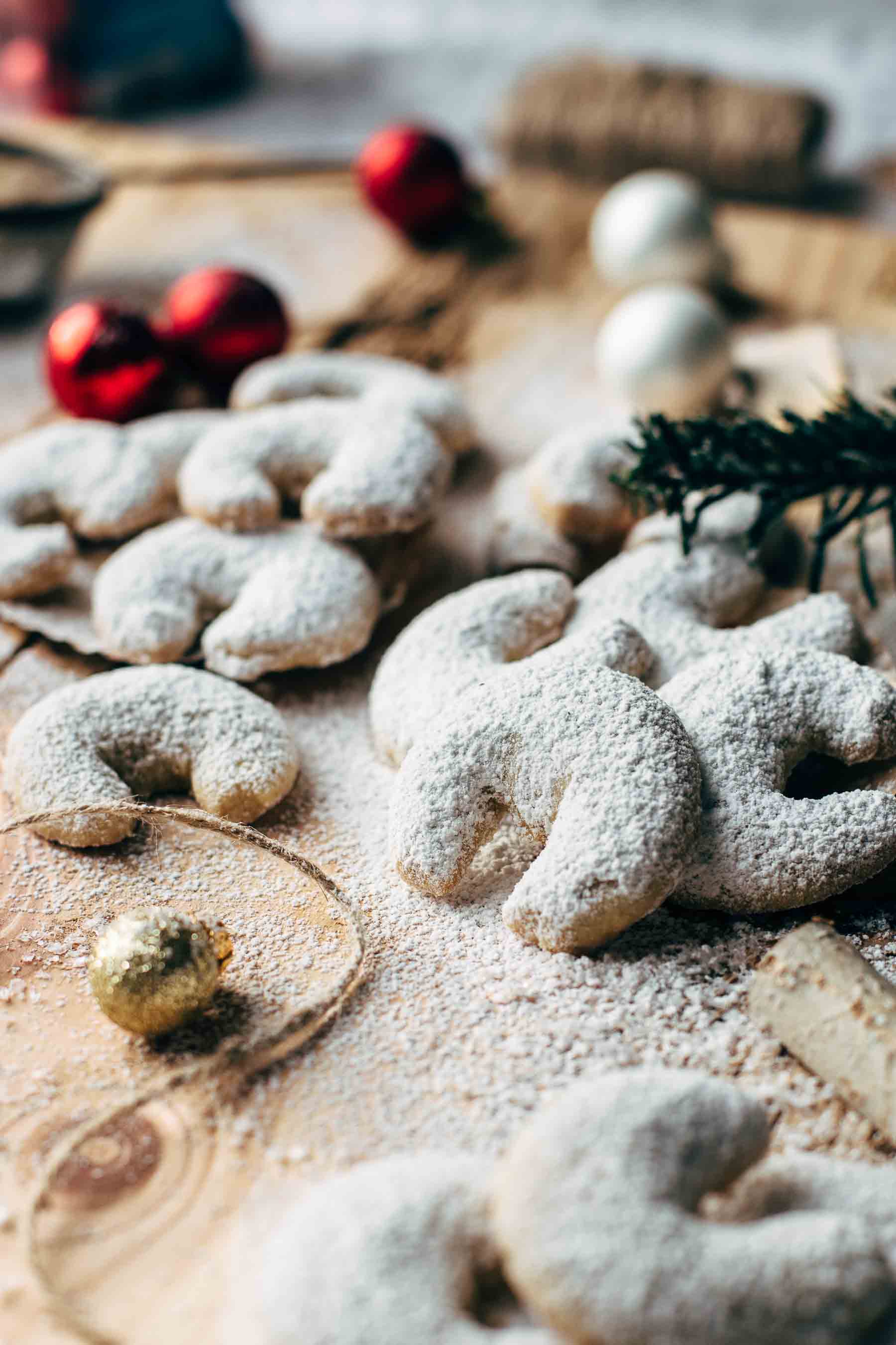 A dozen of vanilla crescent cookies on a wooden table with festive decoration and powdered sugar
