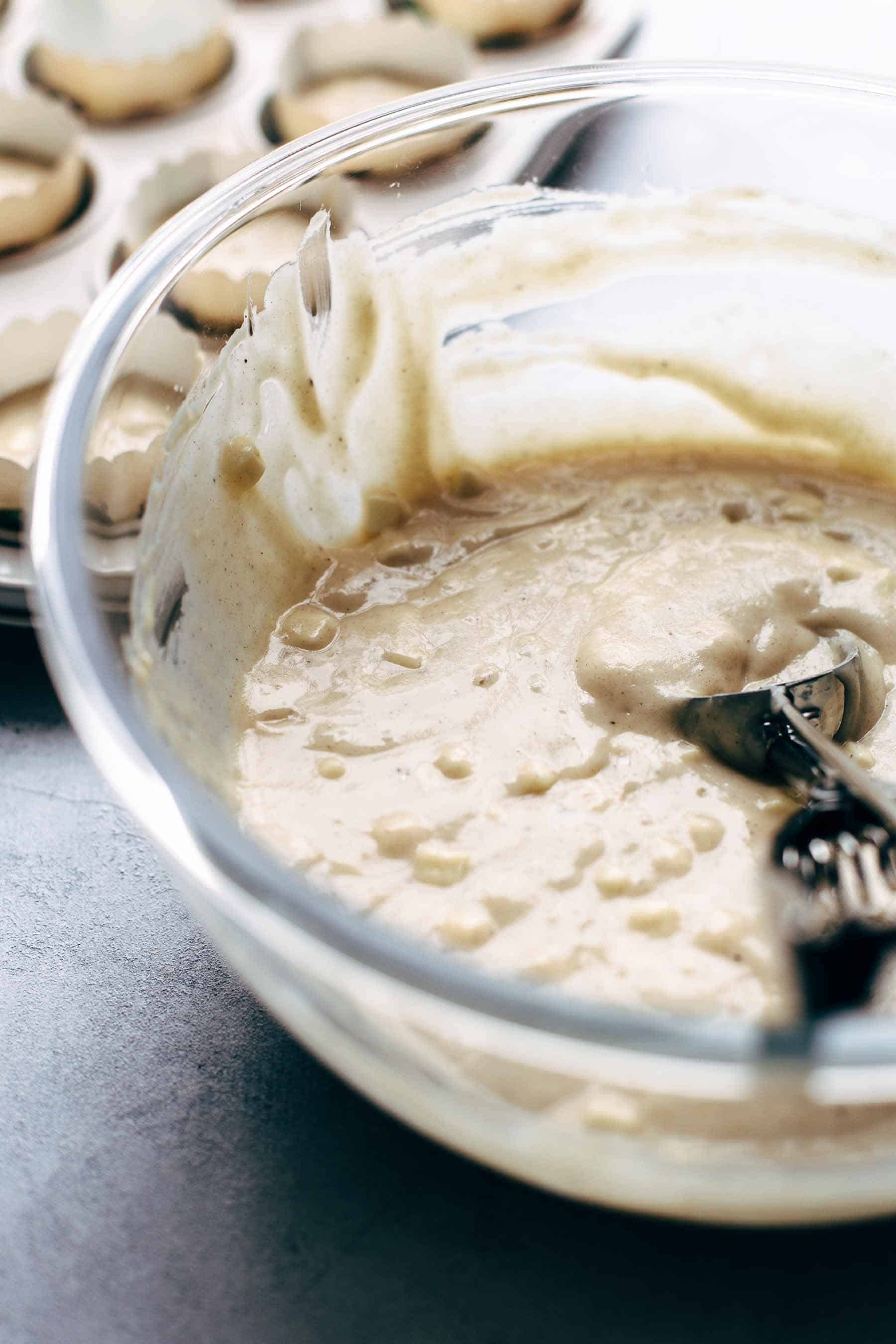 Muffin batter in a large glass mixing bowl with an ice cream scoop in the batter