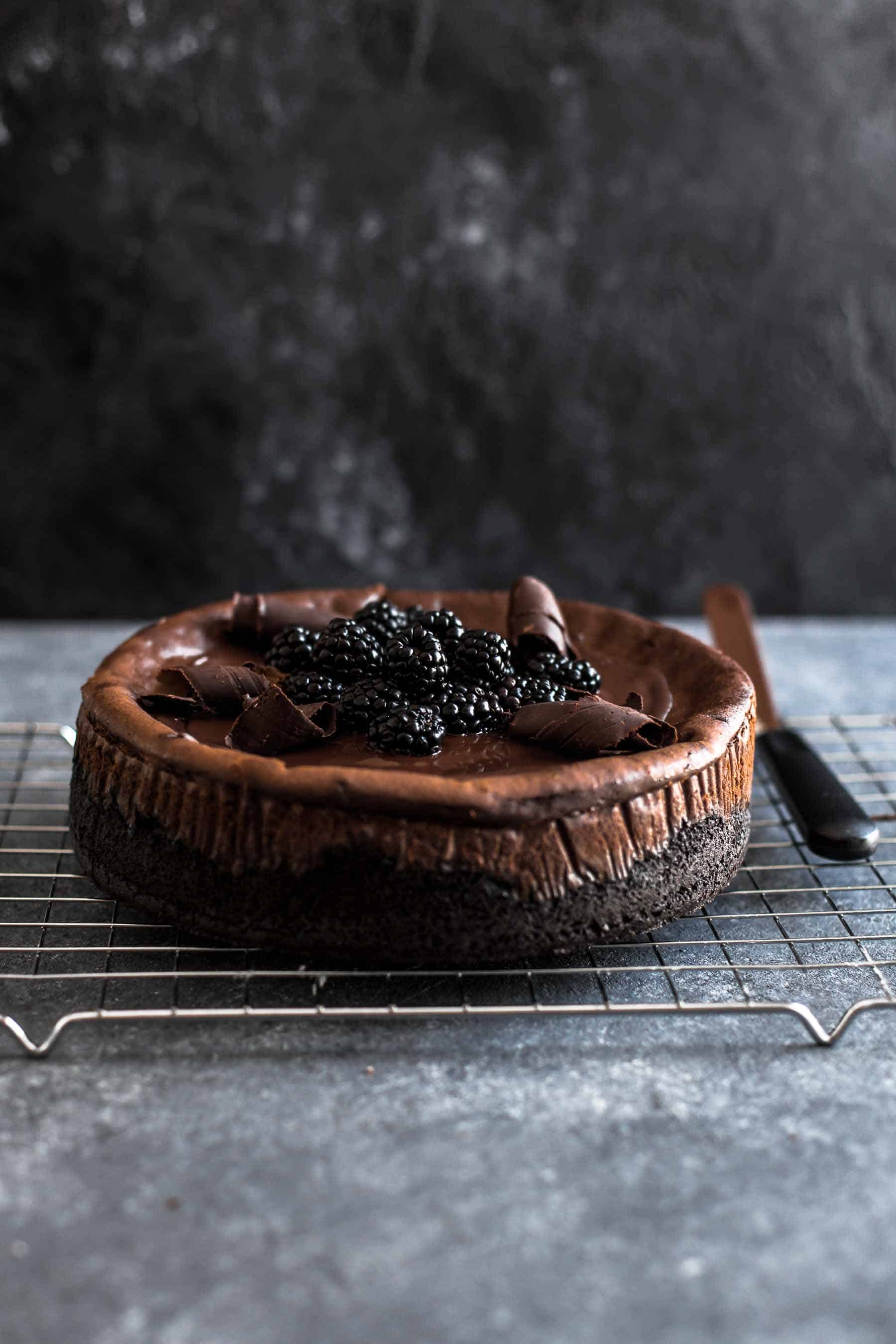 baked chocolate cheesecake on wire rack with Chocolate shavings and blackberries on top