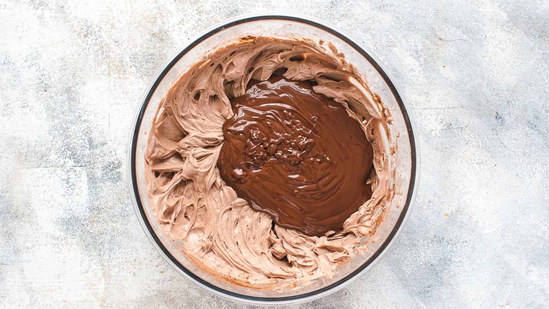 melted chocolate on top of mixed cream cheese in mixing bowl