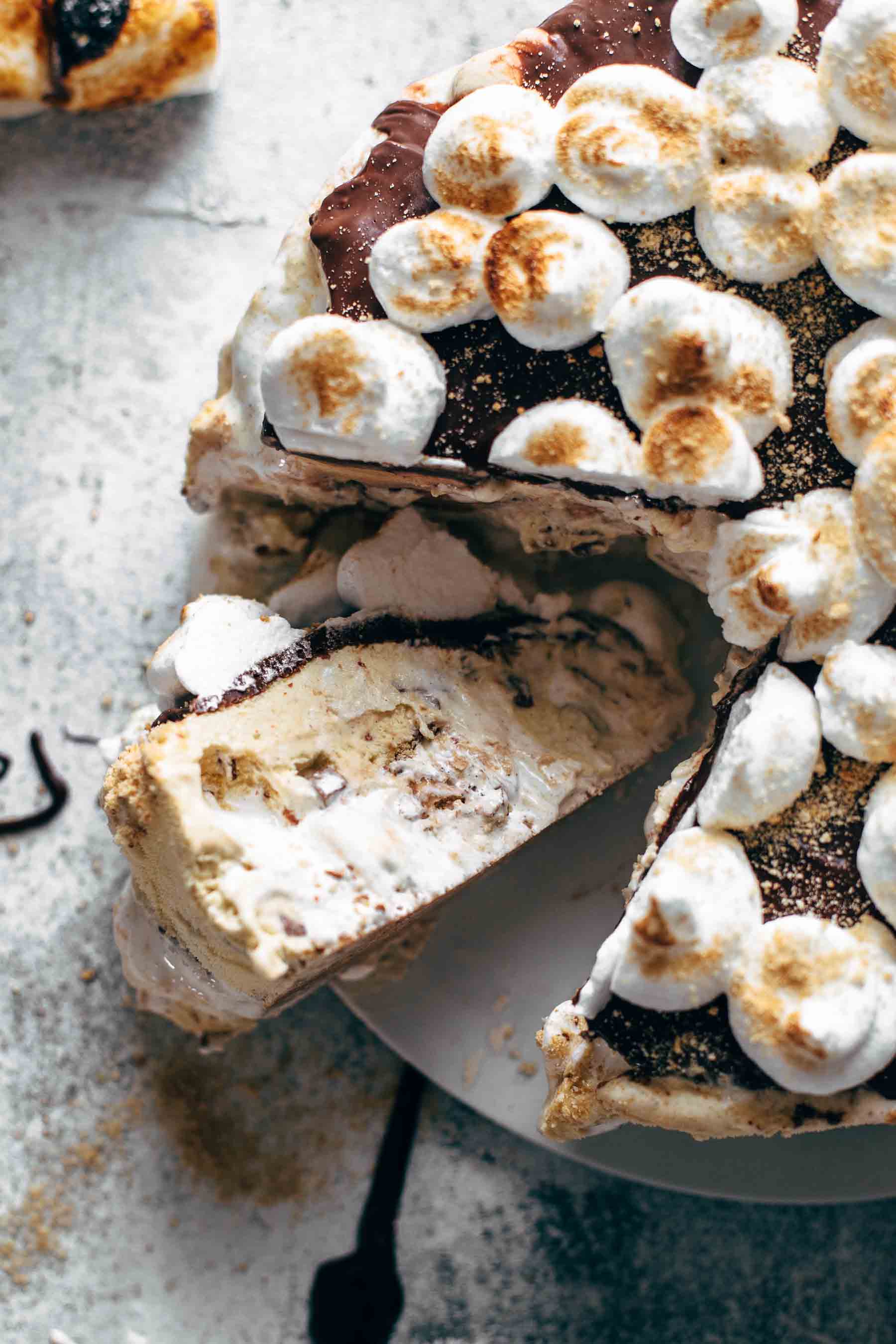 ice cream cake with dollops of meringue on top, one slice is cut out and lightly melting