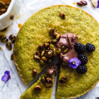 sliced pistachio cake with chocolate, berries, and pistachios on top