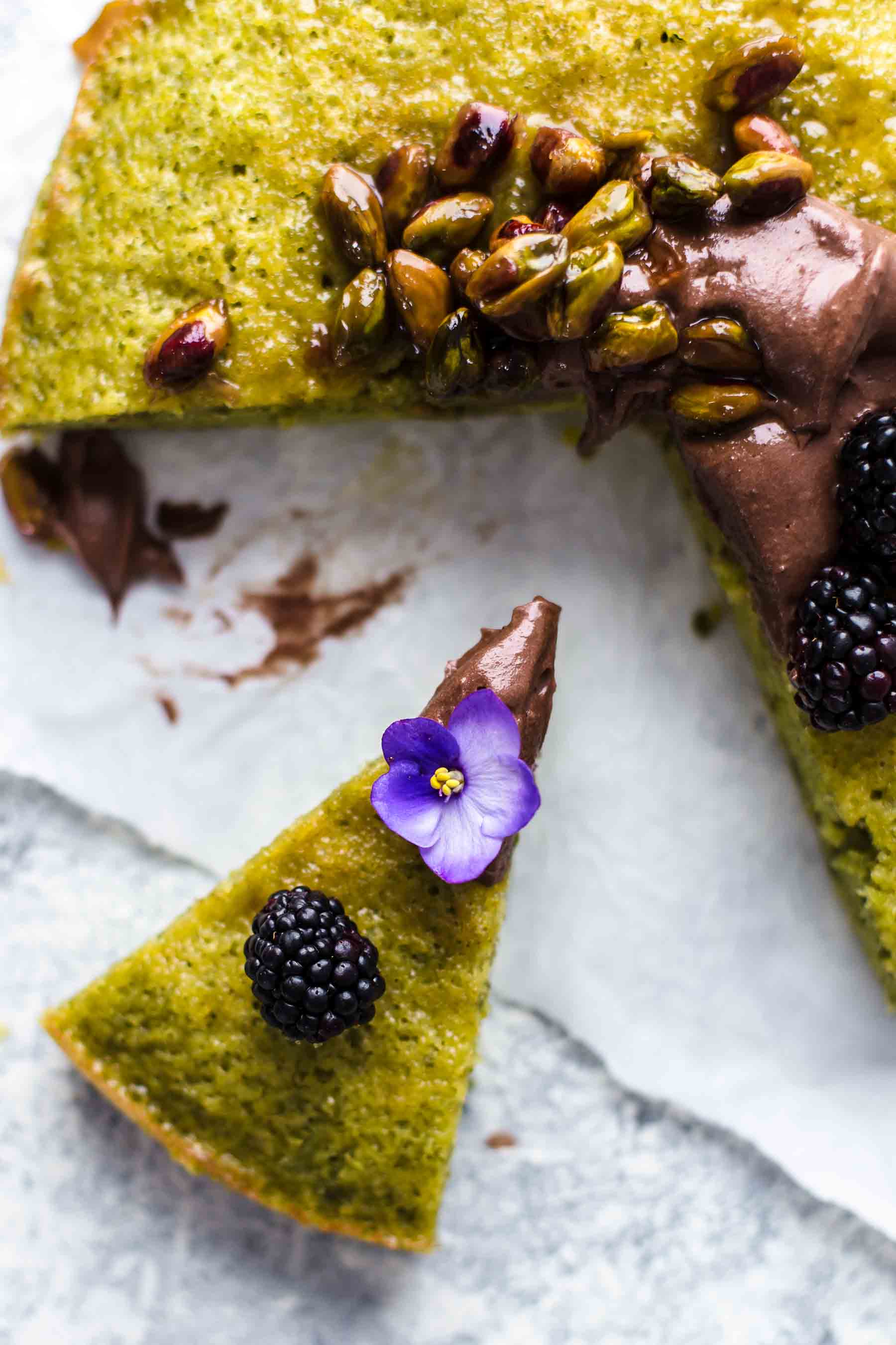 close up of a slice of pistachio cake with a blackberry and flower on top
