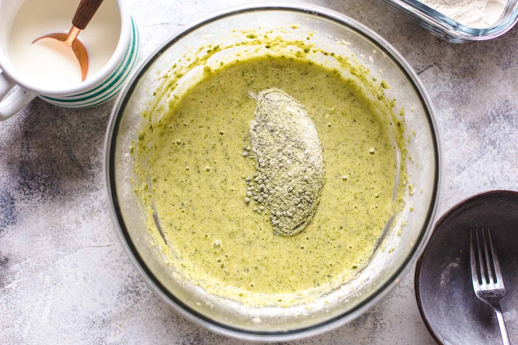 green cake batter with pistachios and dry cake ingredients on top in a bowl