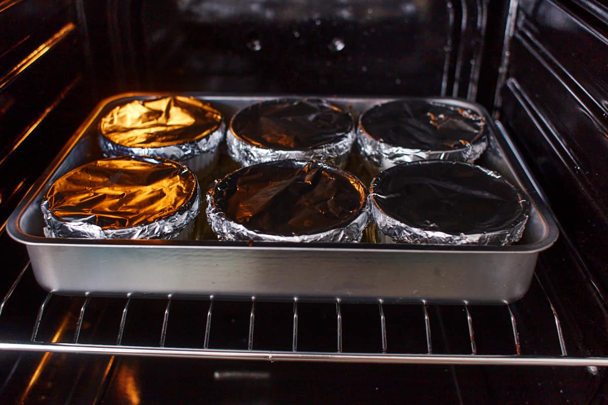 six ramekins covered with aluminum foil in a baking dish sitting in an oven