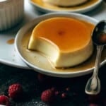two dessert plates with flan and thin sugar syrup with one having a bite taken out with a spoon