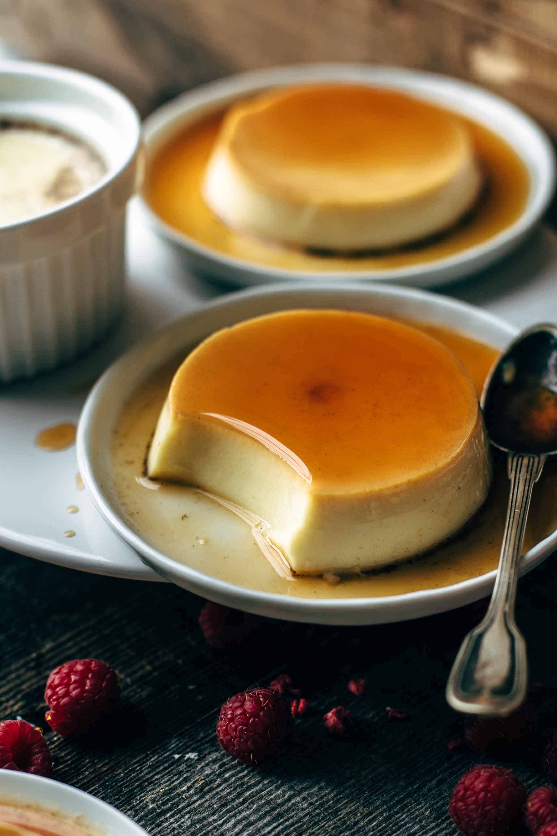 two dessert plates with flan and thin sugar syrup with one having a bite taken out with a spoon