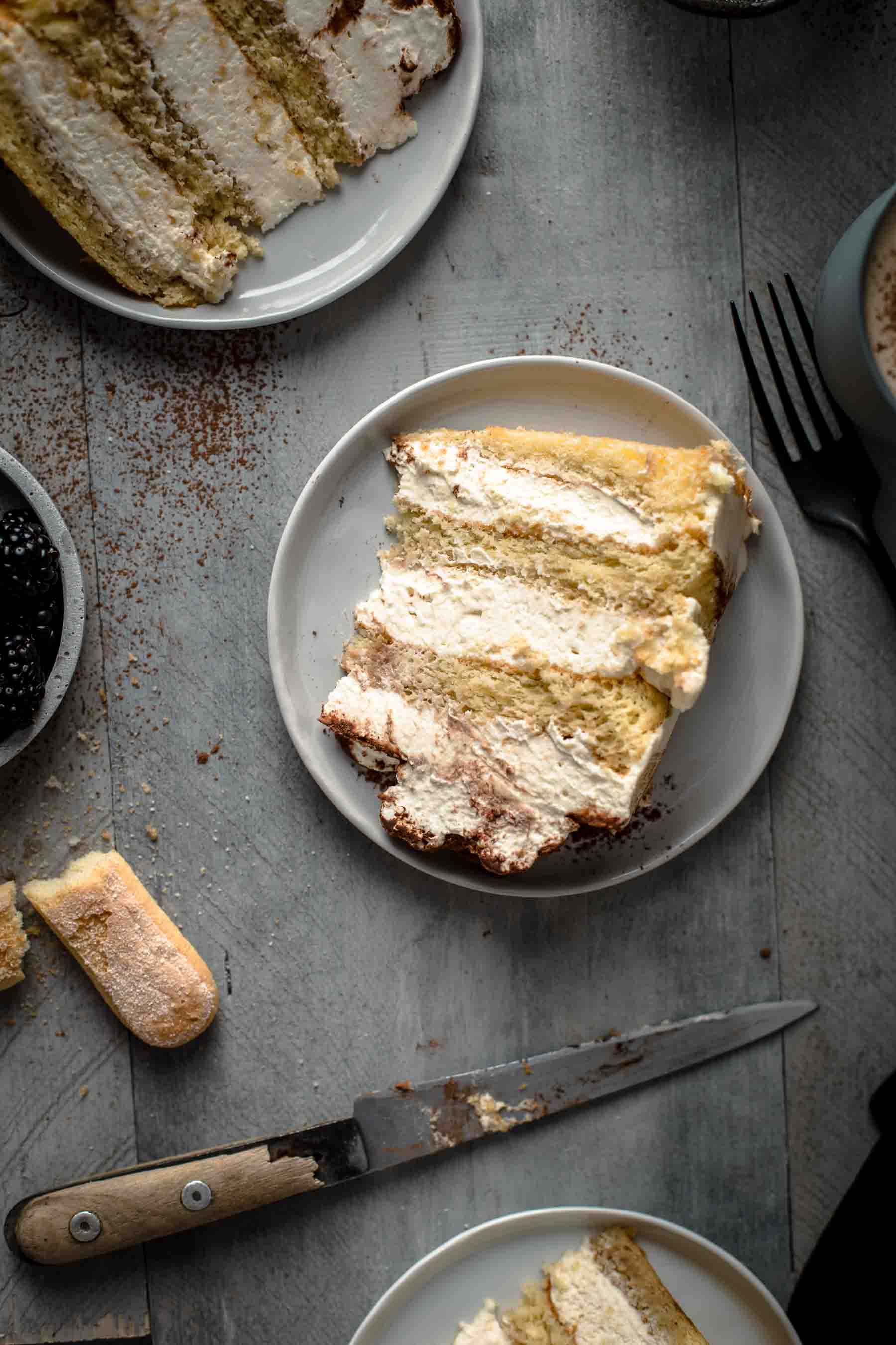 a slice of tiramisu cake on a serving plate with a knife and fork next to it