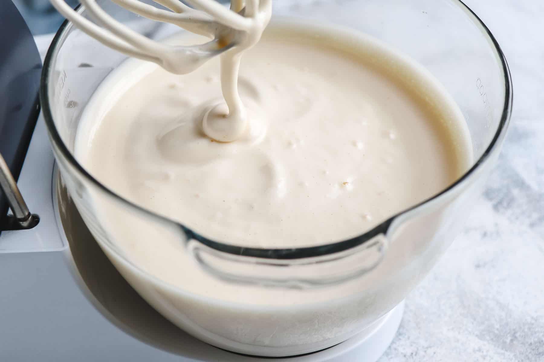 whipped batter in a bowl with batter dripping down the whisk attachment