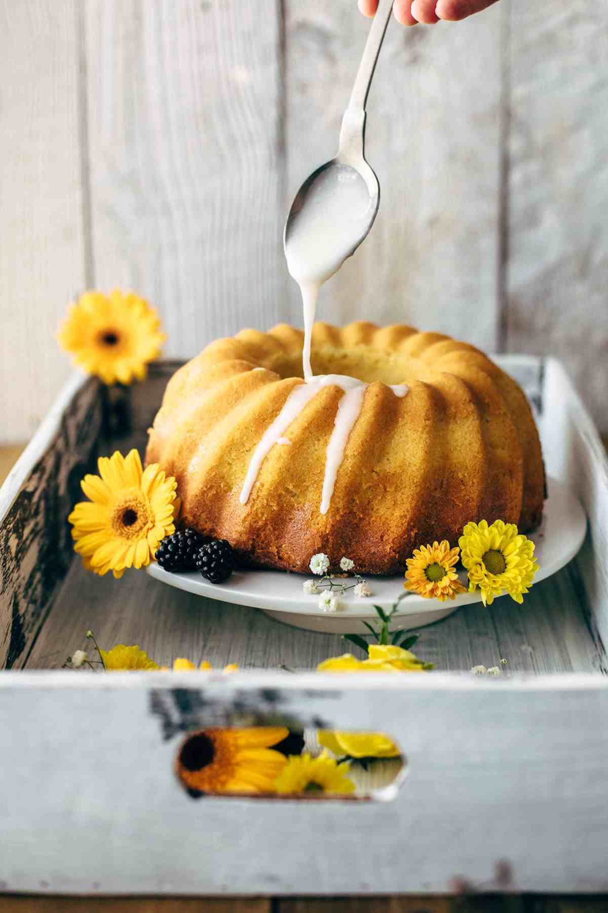 Drizzling icing over lemon bundt cake on a cake stand