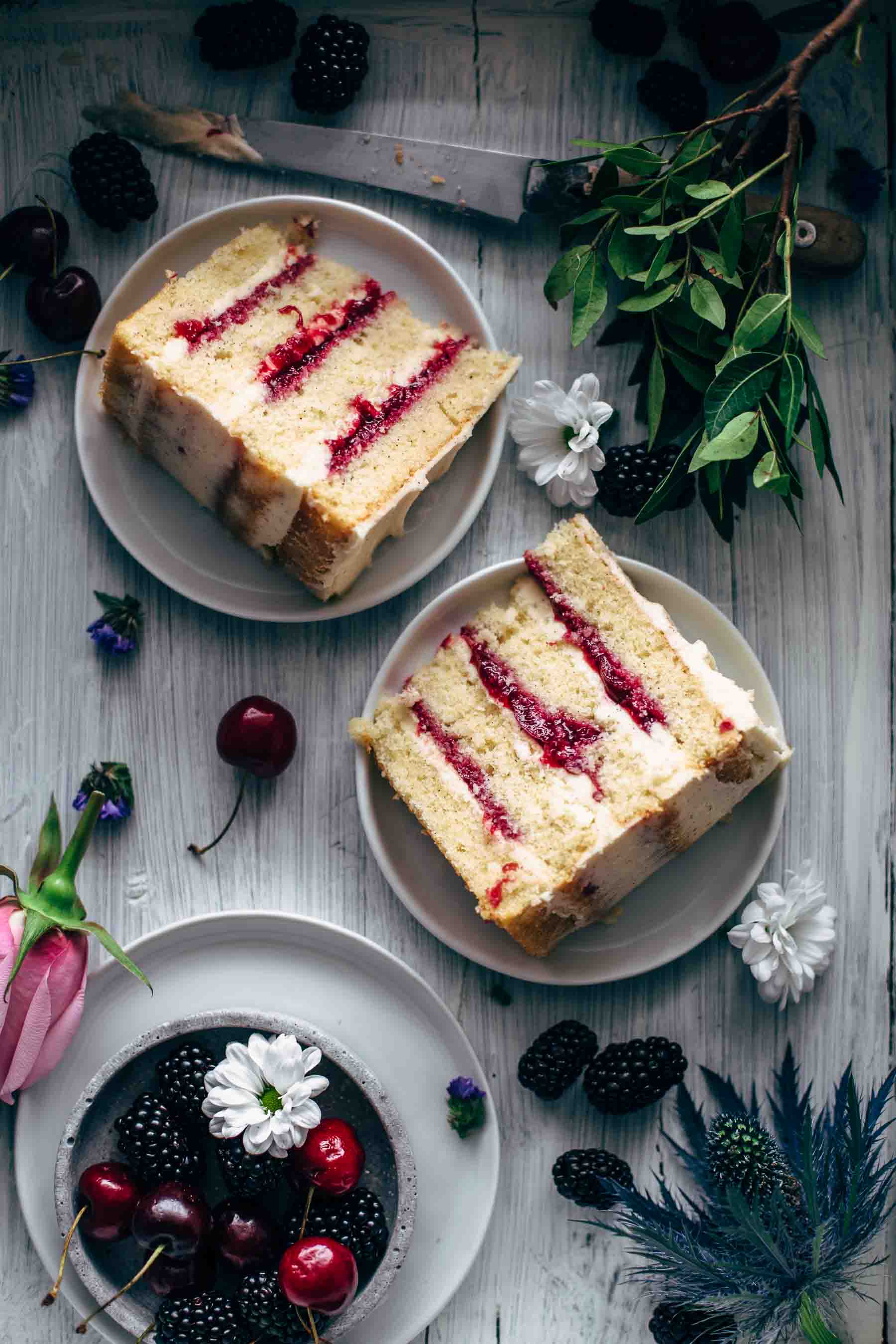 Two slices of cherry layer cake on two serving plates with flower and fruit decoration