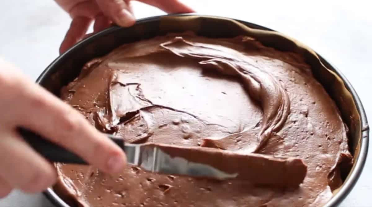 no-bake chocolate cheesecake filling being spread out on a springform pan with cookie crust