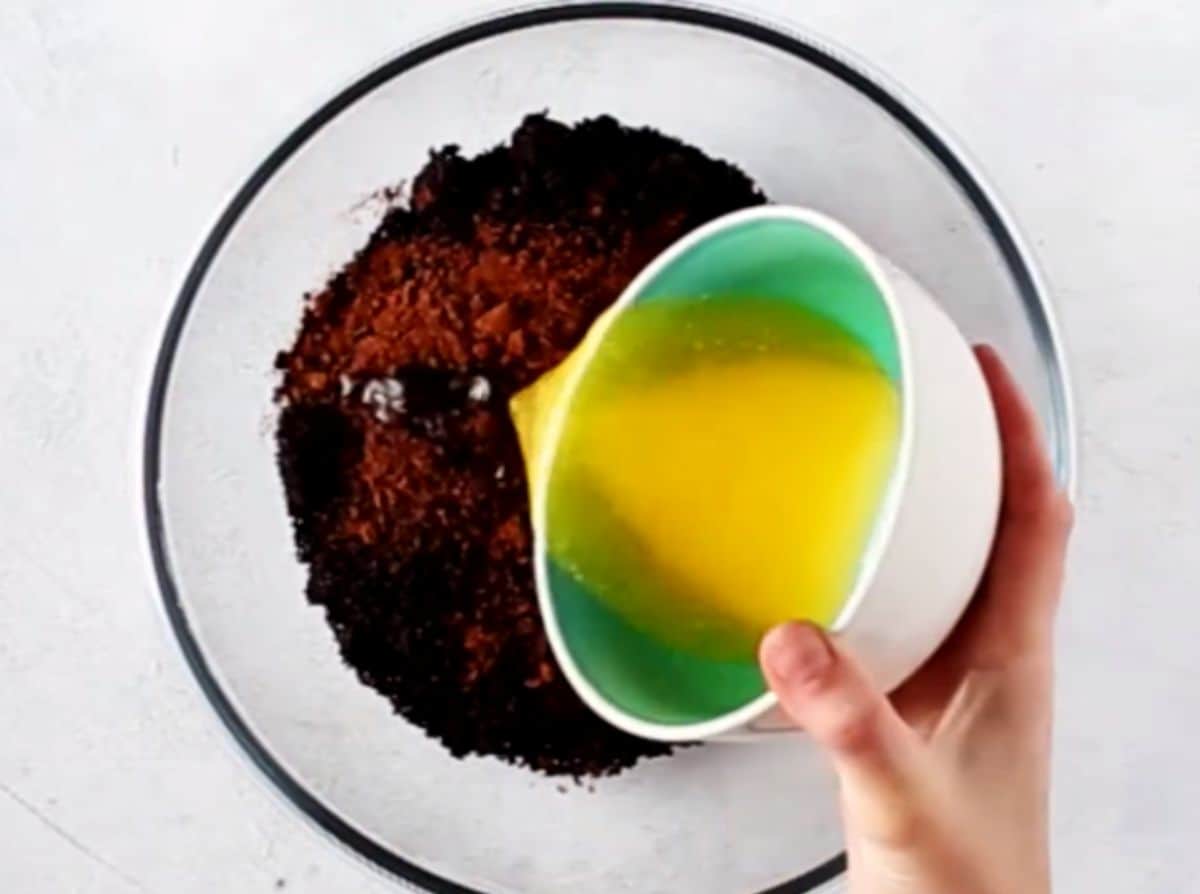 Pouring butter on fine chocolate cookie crumbs.