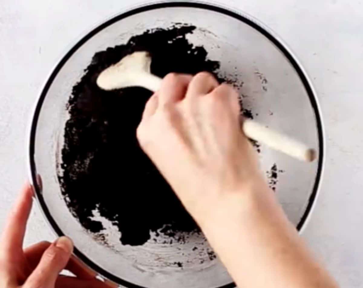 mixing chocolate crust for no-bake chocolate cheesecake in a glass bowl