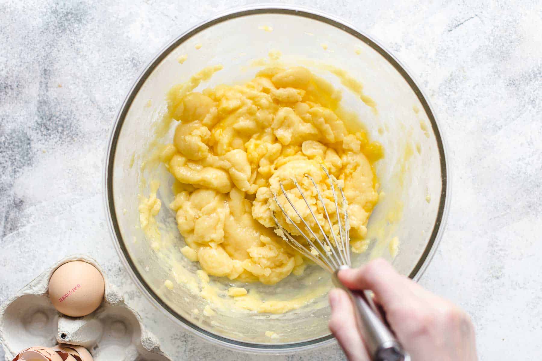 incorporating eggs into a sticky dough with a whisk