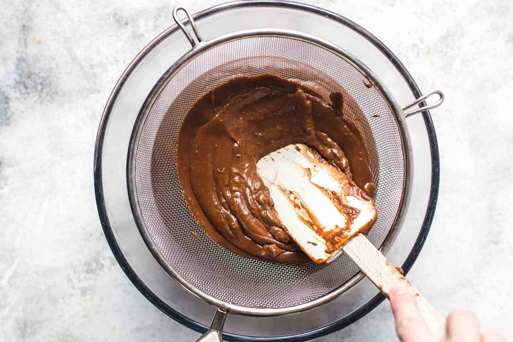 pressing chocolate cream through mesh strainer with a spatula