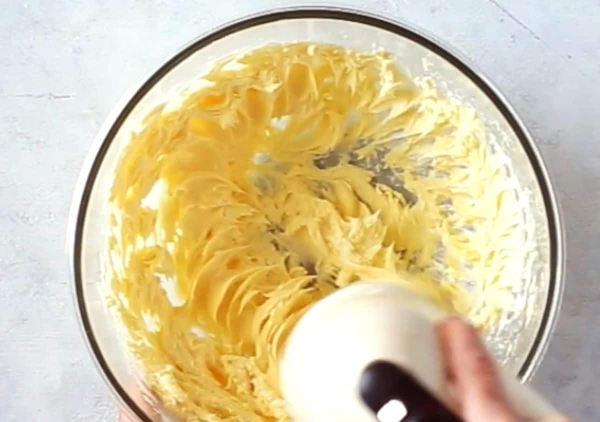 beating buttercream frosting using a hand mixer in a glass bowl