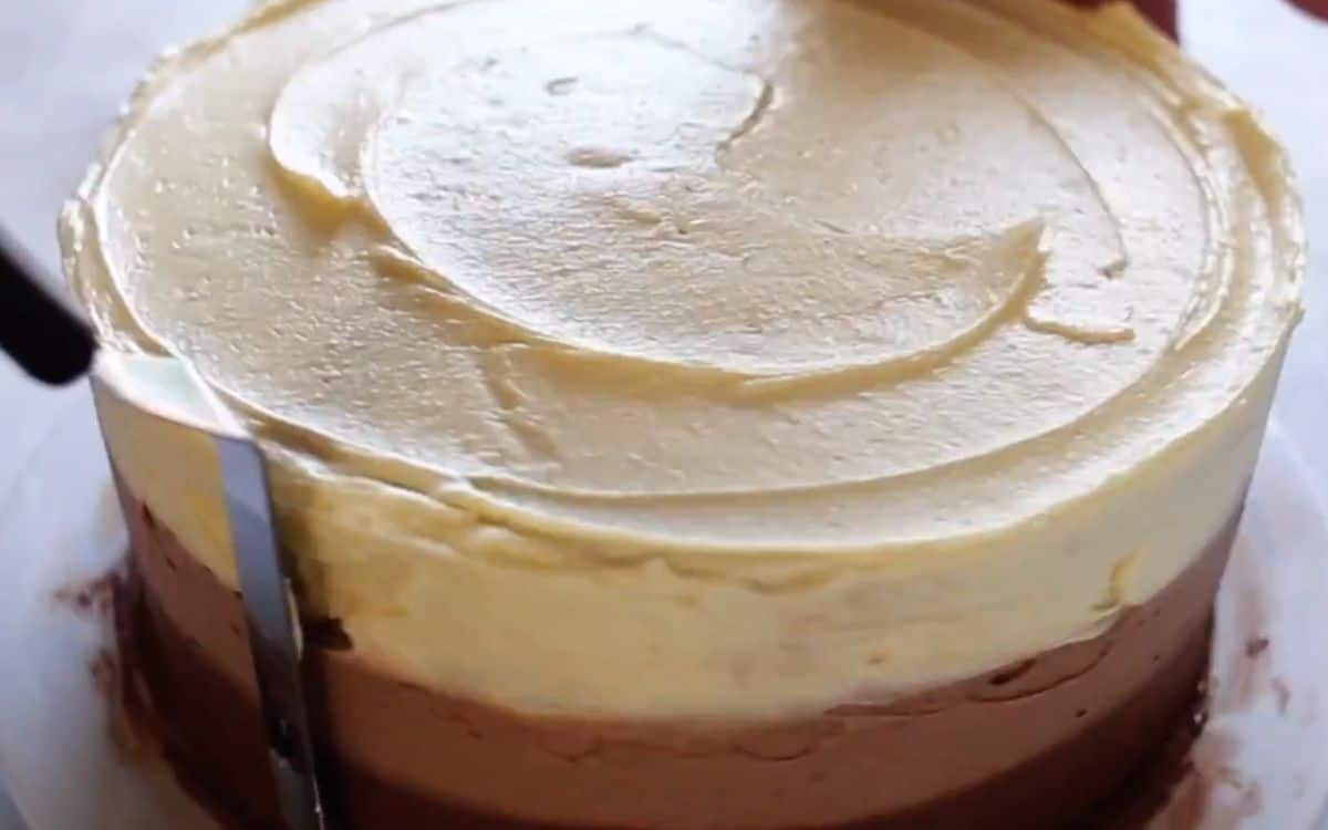 applying pale buttercream frosting to whole cake