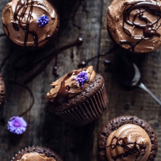 half dozen brownie cupcakes with chocolate syrup and flower decoration on a wooden table
