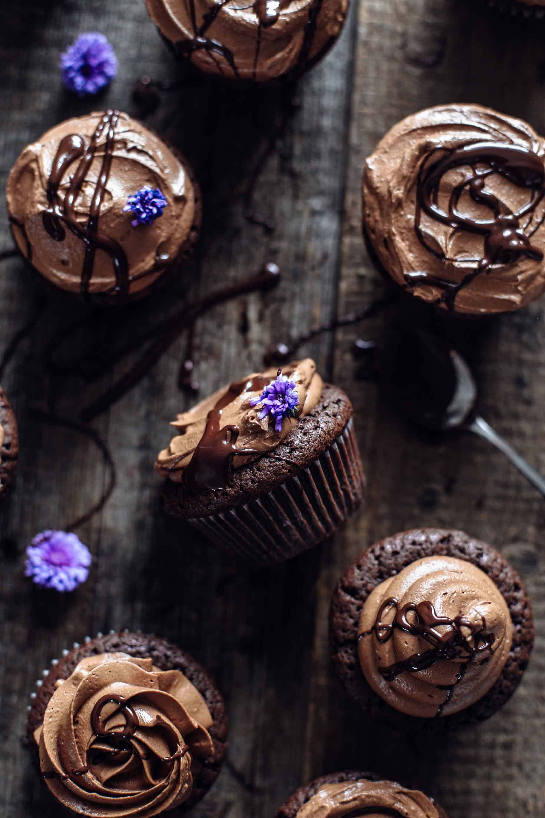 half dozen brownie cupcakes with chocolate syrup and flower decoration on a wooden table