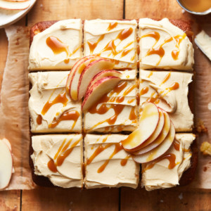 Sliced apple cake topped with frosting, caramel sauce, and apple slices on a table