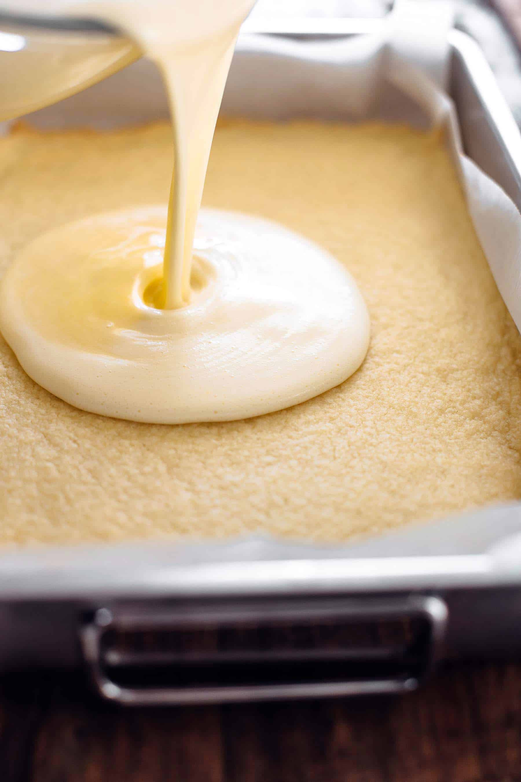 Pouring lemon curd on top pre-baked shortbread crust in baking pan