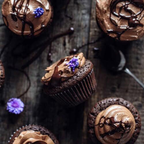 Brownie cupcakes on a wooden background garnished with purple flowers.