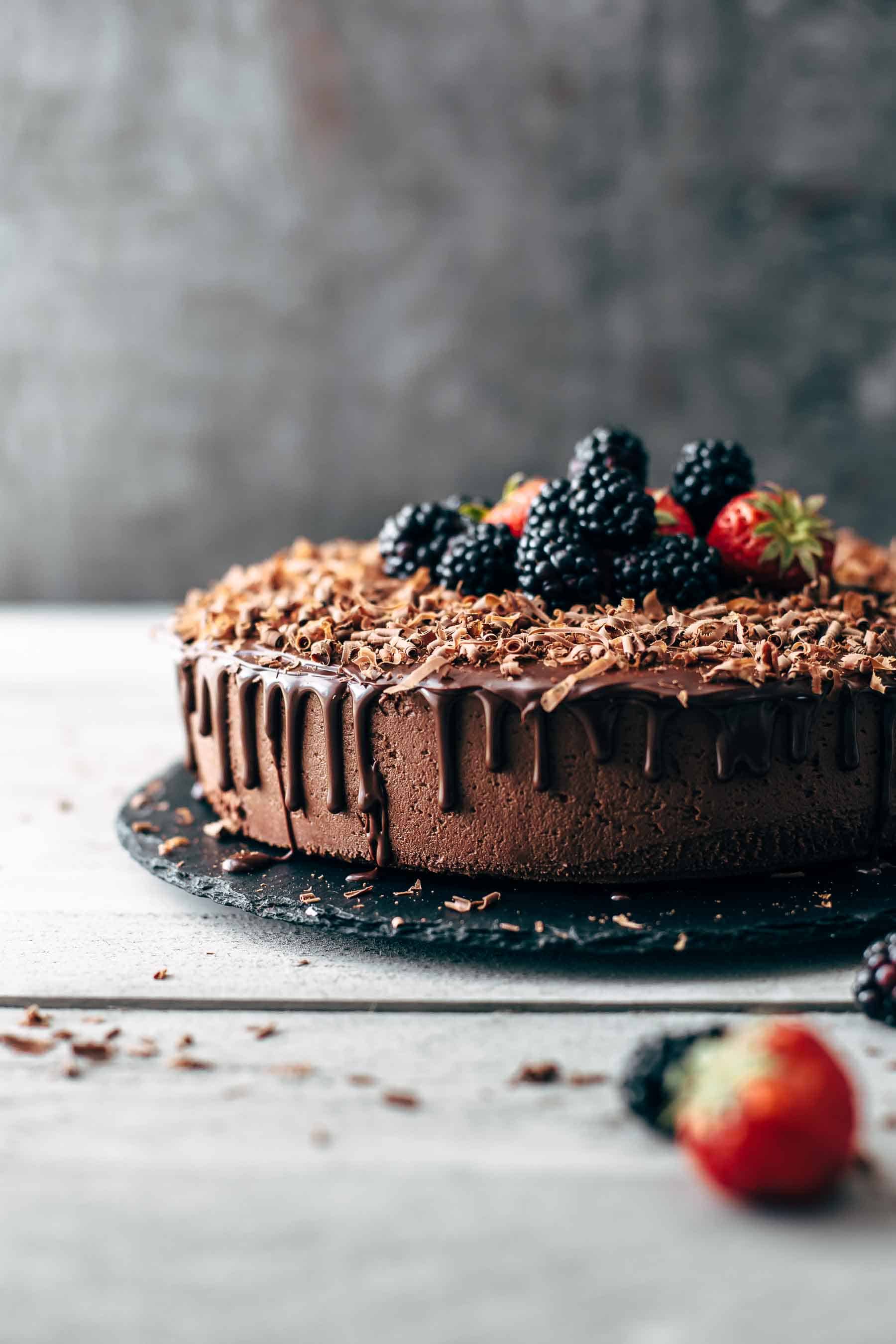 chocolate cake with ganache dripping down the sides, topped with berries and chocolate shavings