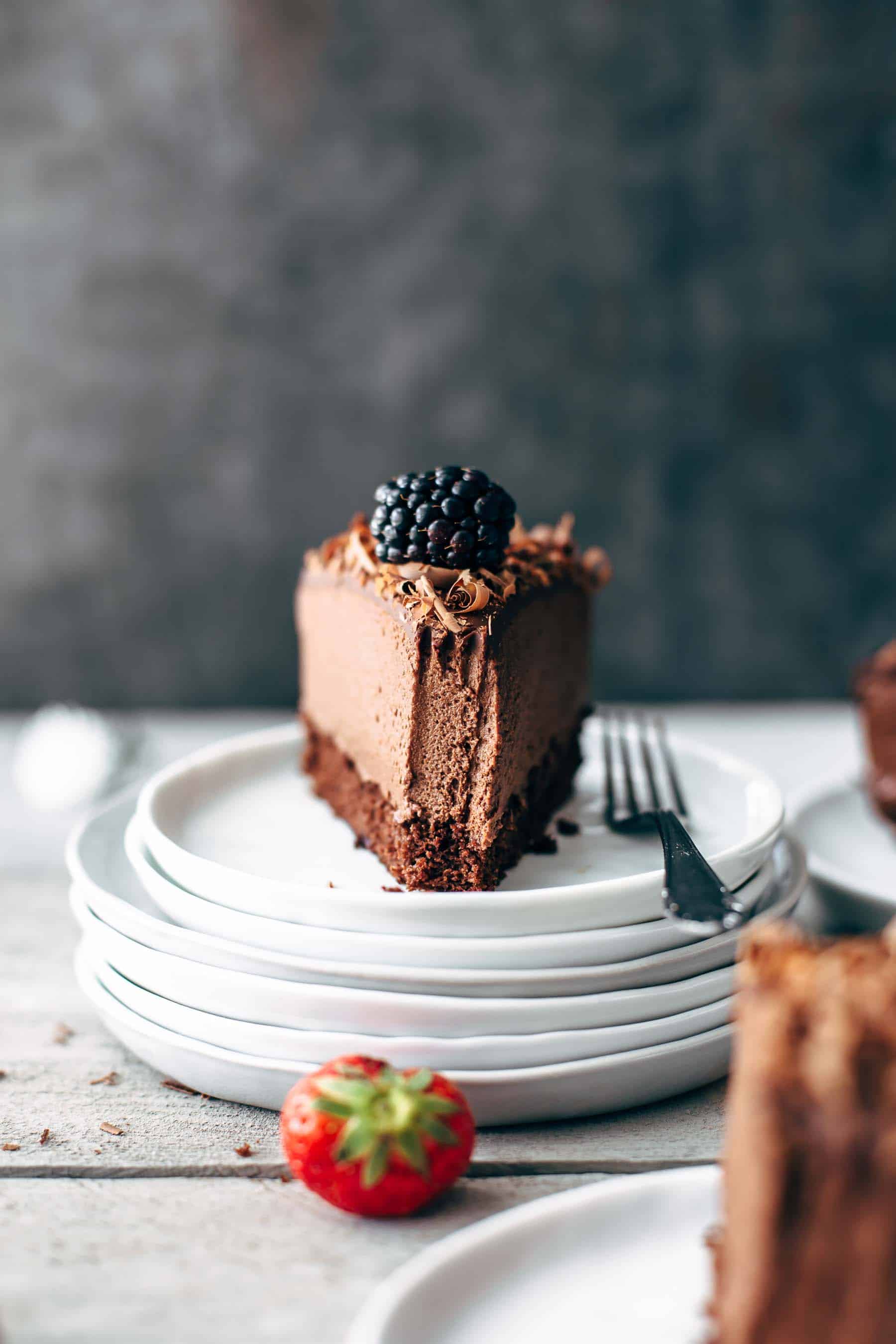 a slice of chocolate cake with a blackberry on top on a pile of stacked dessert plates