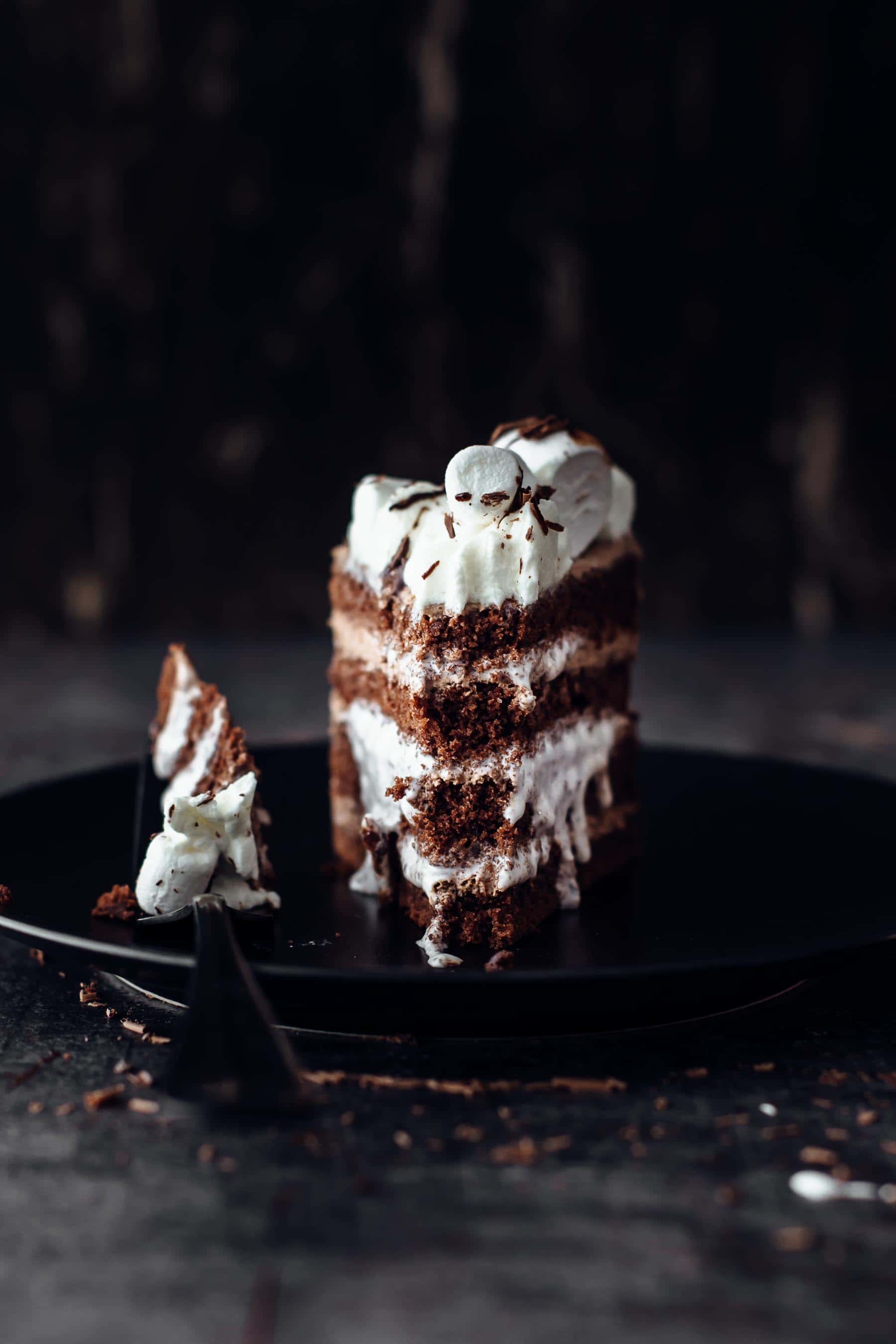 a slice of chocolate marshmallow cake with a bite taken out on a black dessert plate