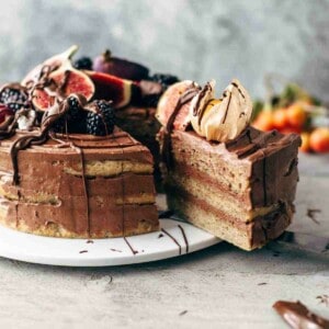 sliced banana layer cake topped with chocolate frosting and fresh fruit on a cake plate