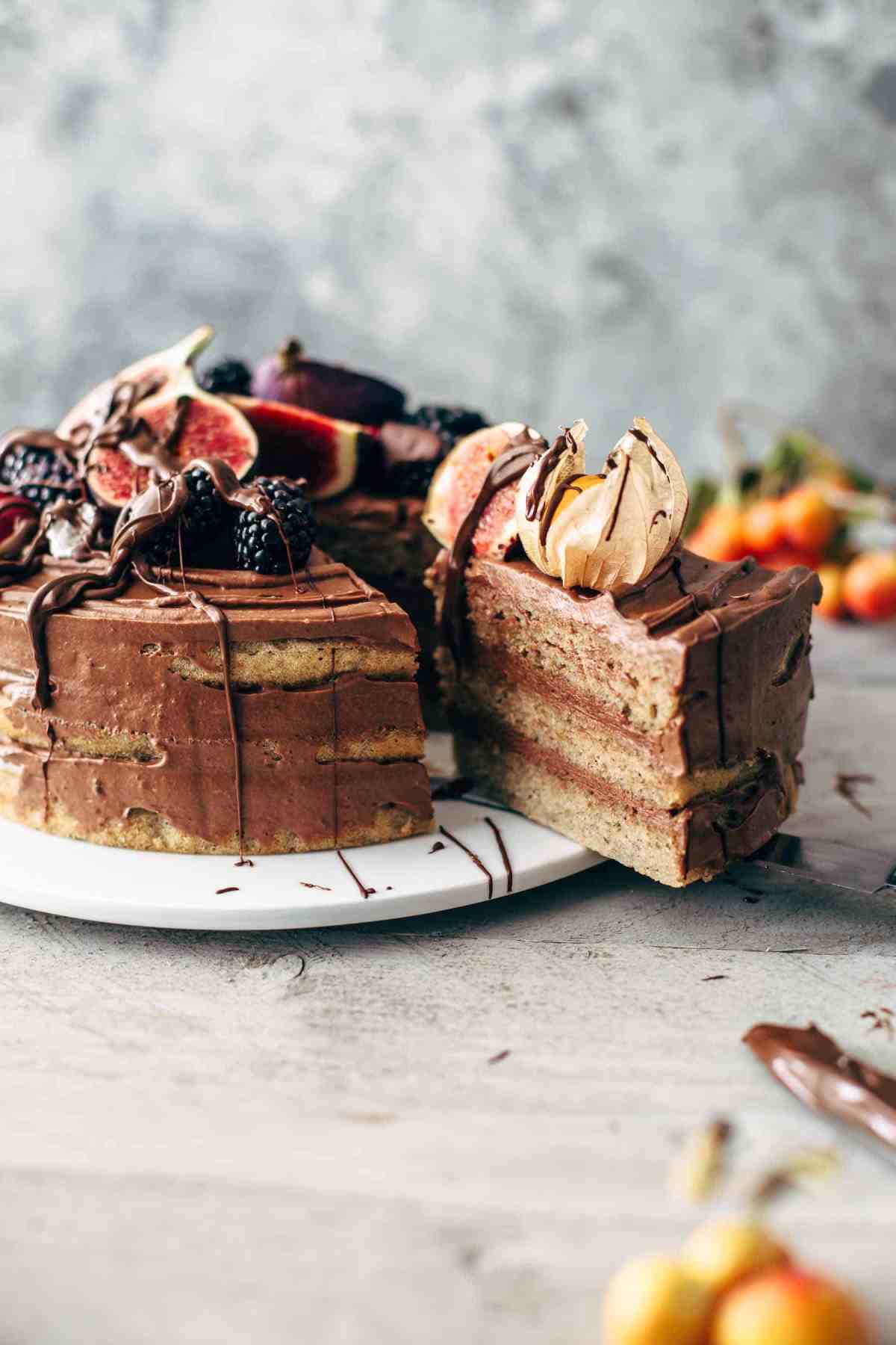 sliced banana layer cake topped with chocolate frosting and fresh fruit on a cake plate