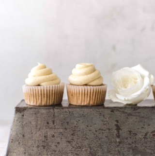 Two banana cupcakes on a baking tin with a white rose next to them