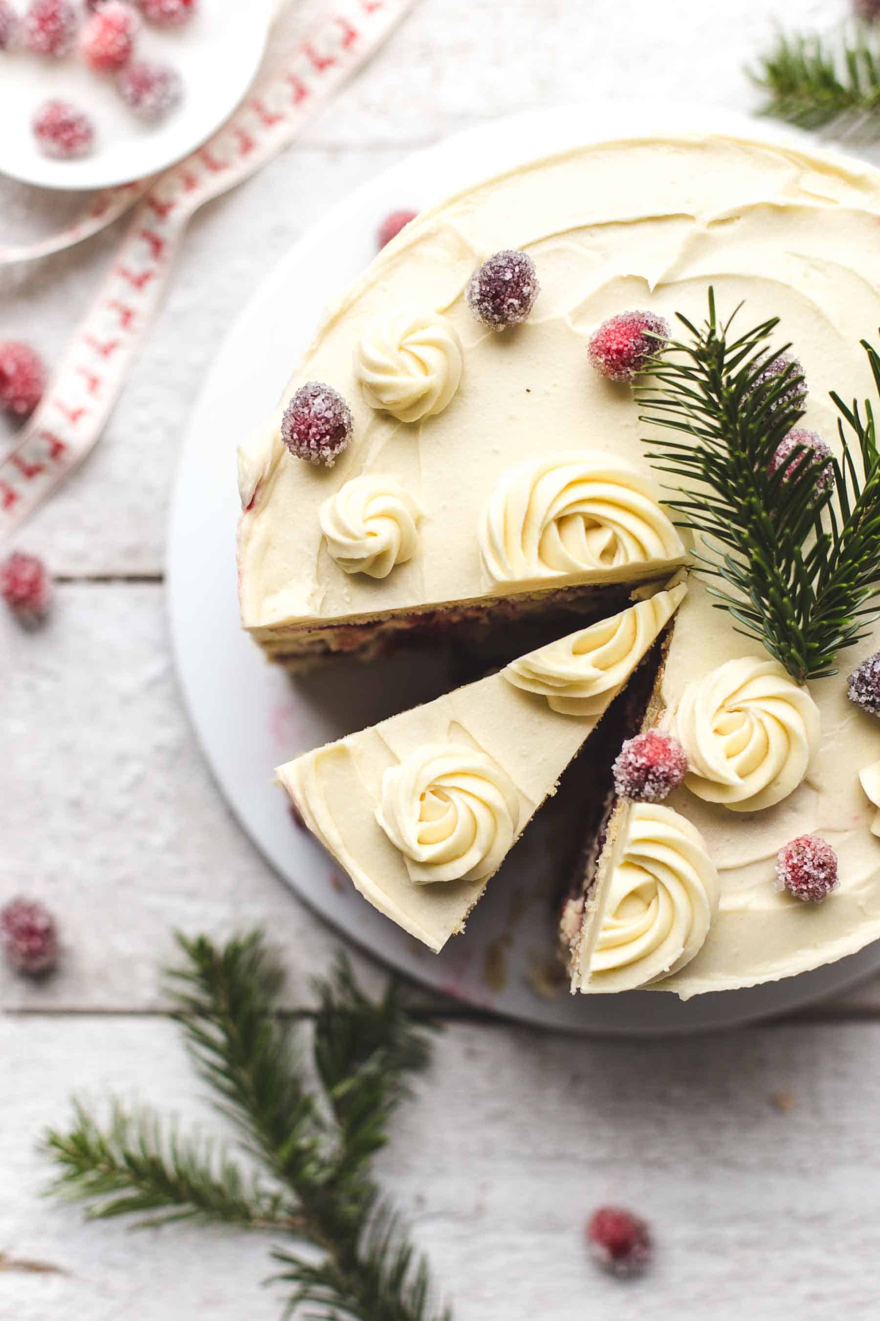 sliced orange cranberry cake with frosting and sugared cranberries on top