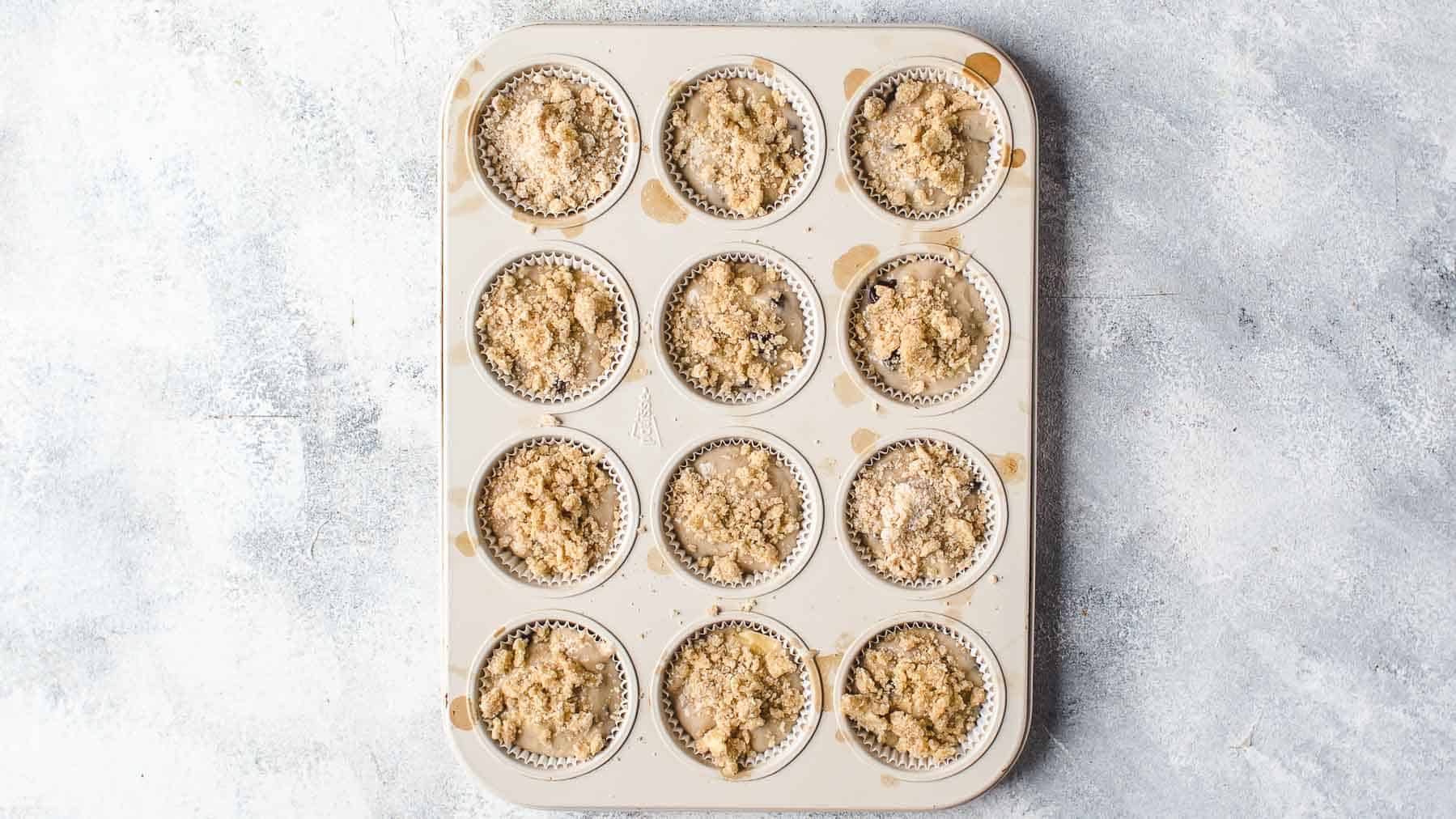 muffin batter with streusel topping in muffin liners in a pan