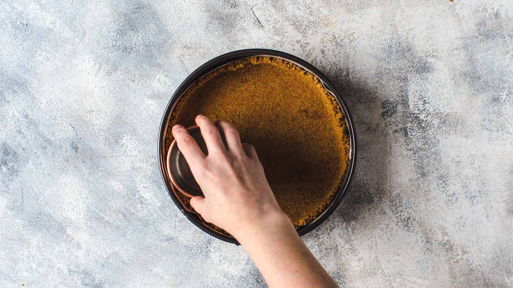 pressing graham cracker crust into the bottom of a springform pan with the back of a cup