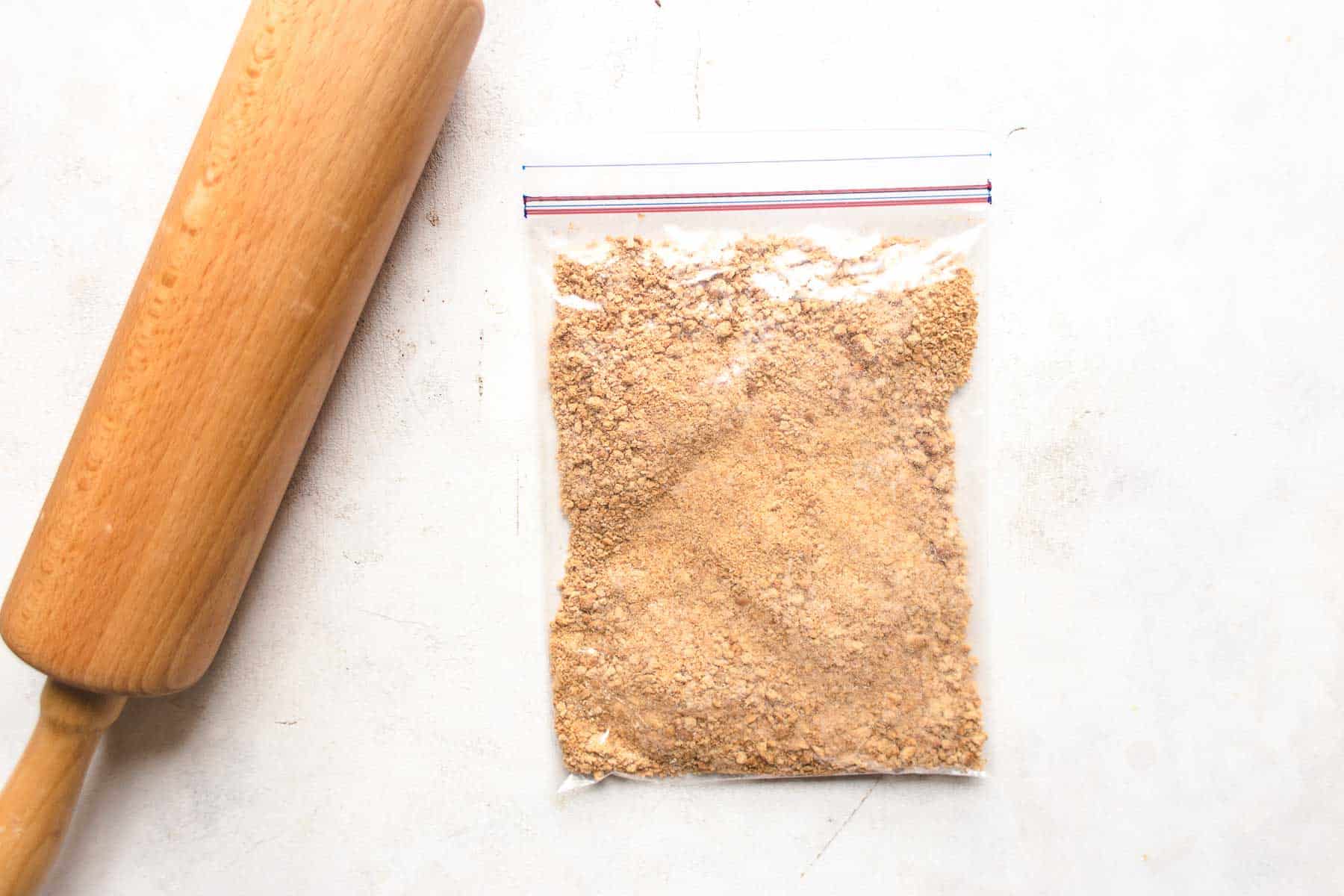 graham cracker crumbs in plastic bag with rolling pin next to it