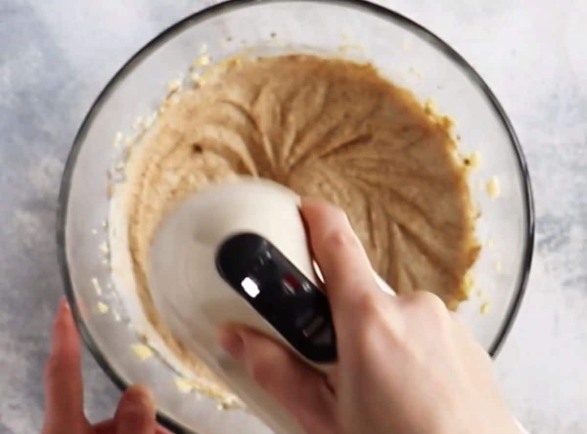 mixing coffee cupcake batter in glass bowl using hand mixer