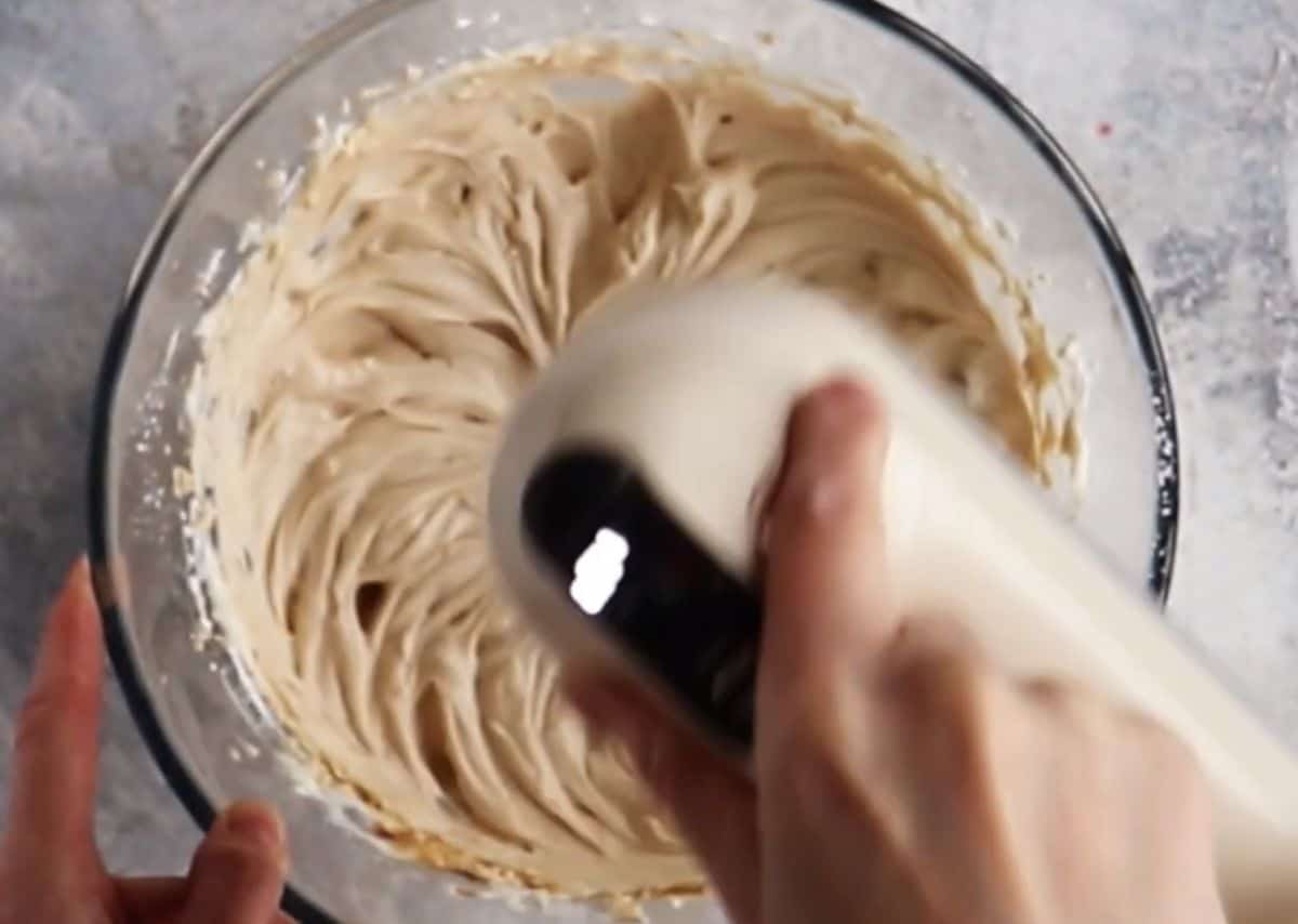 beating mascarpone with brewed coffee in a glass bowl using hand mixer