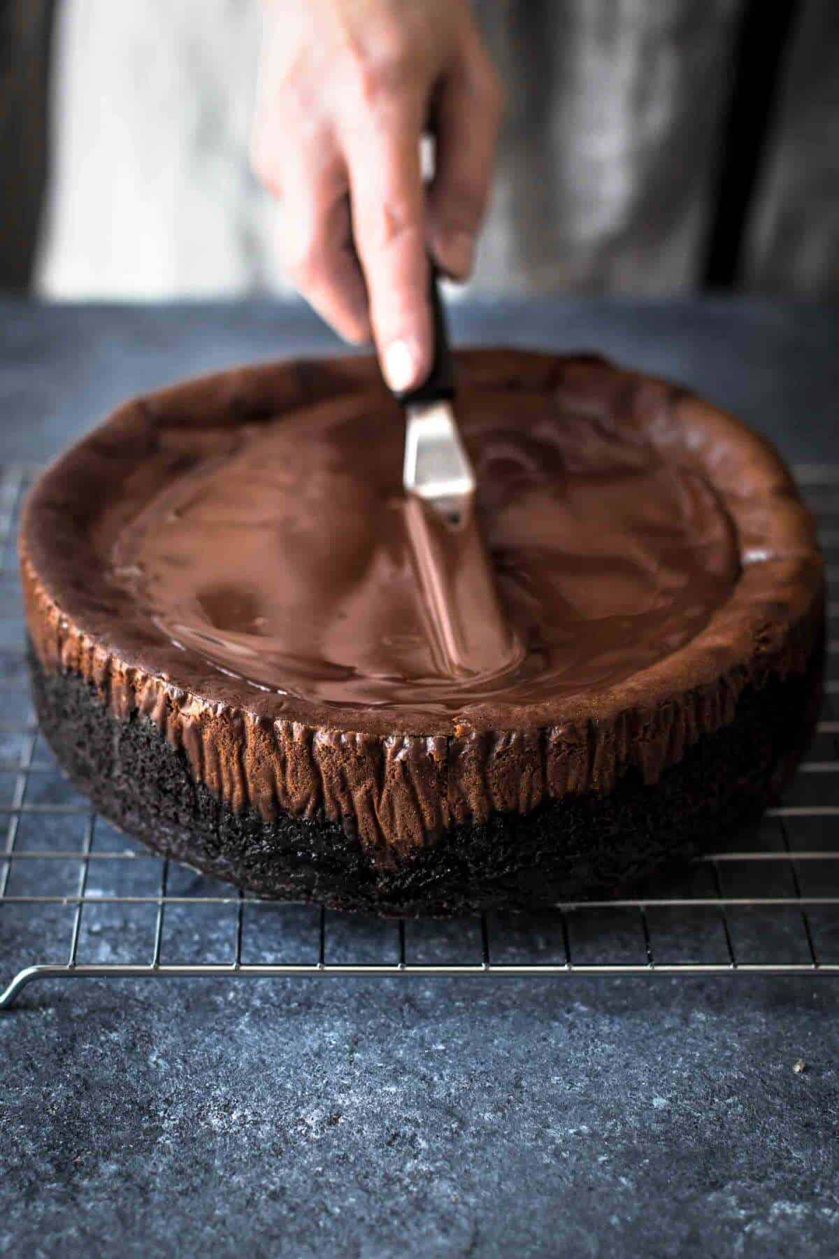 spreading chocolate ganache on top of chocolate cheesecake