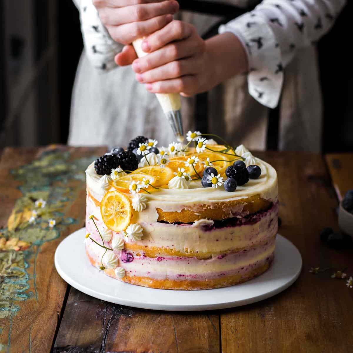 Decorating a lemon blueberry cake with frosting, fruits, and flowers