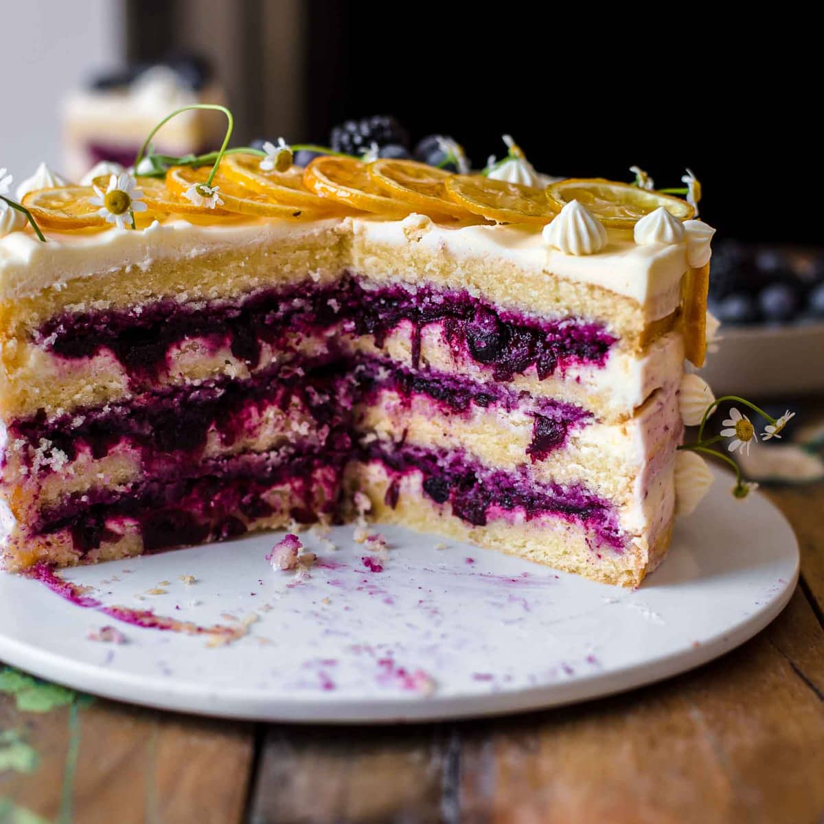 Lemon layer cake with blueberry filling on a white serving plate with one third of the cake missing