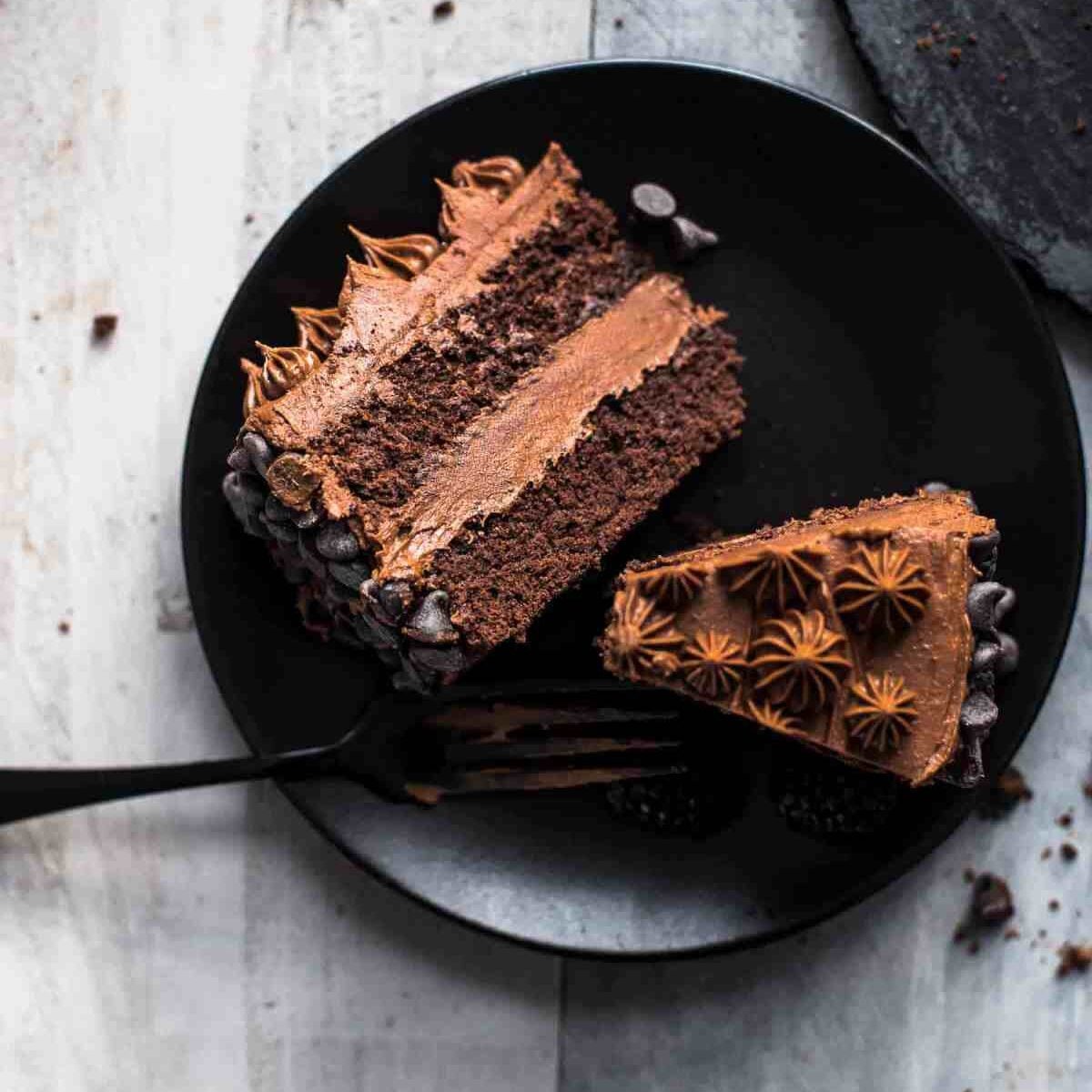 two slices of chocolate cake on a black serving plate with a fork