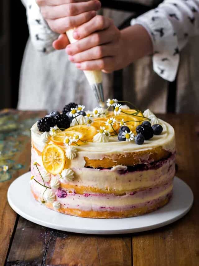 Decorating a lemon blueberry cake with frosting, fruits, and flowers
