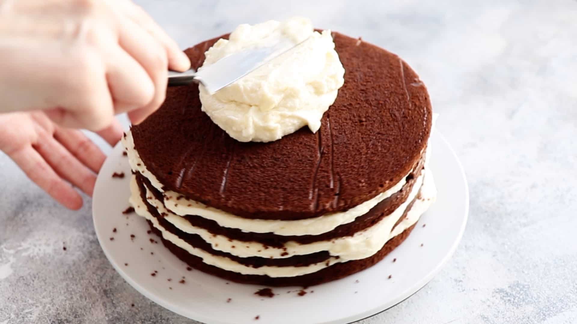 spreading coconut frosting over chocolate cake layers with offset spatula