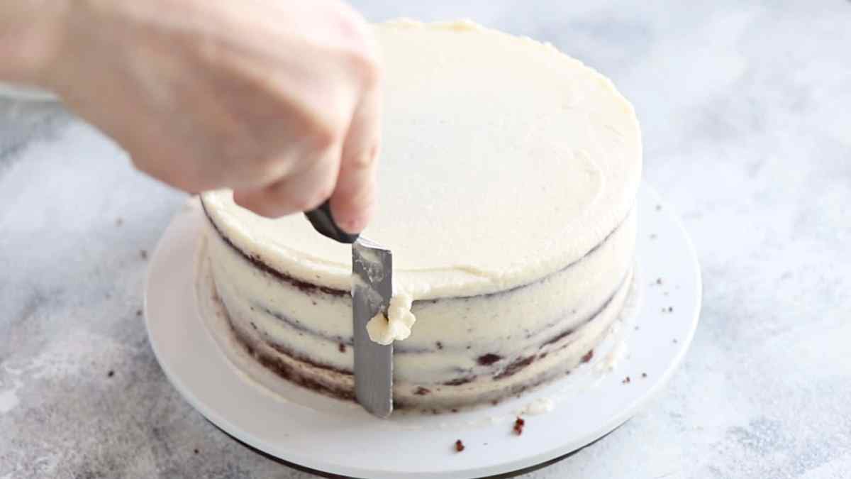 Leveling the sides of the chocolate cake with coconut frosting with an offset spatula