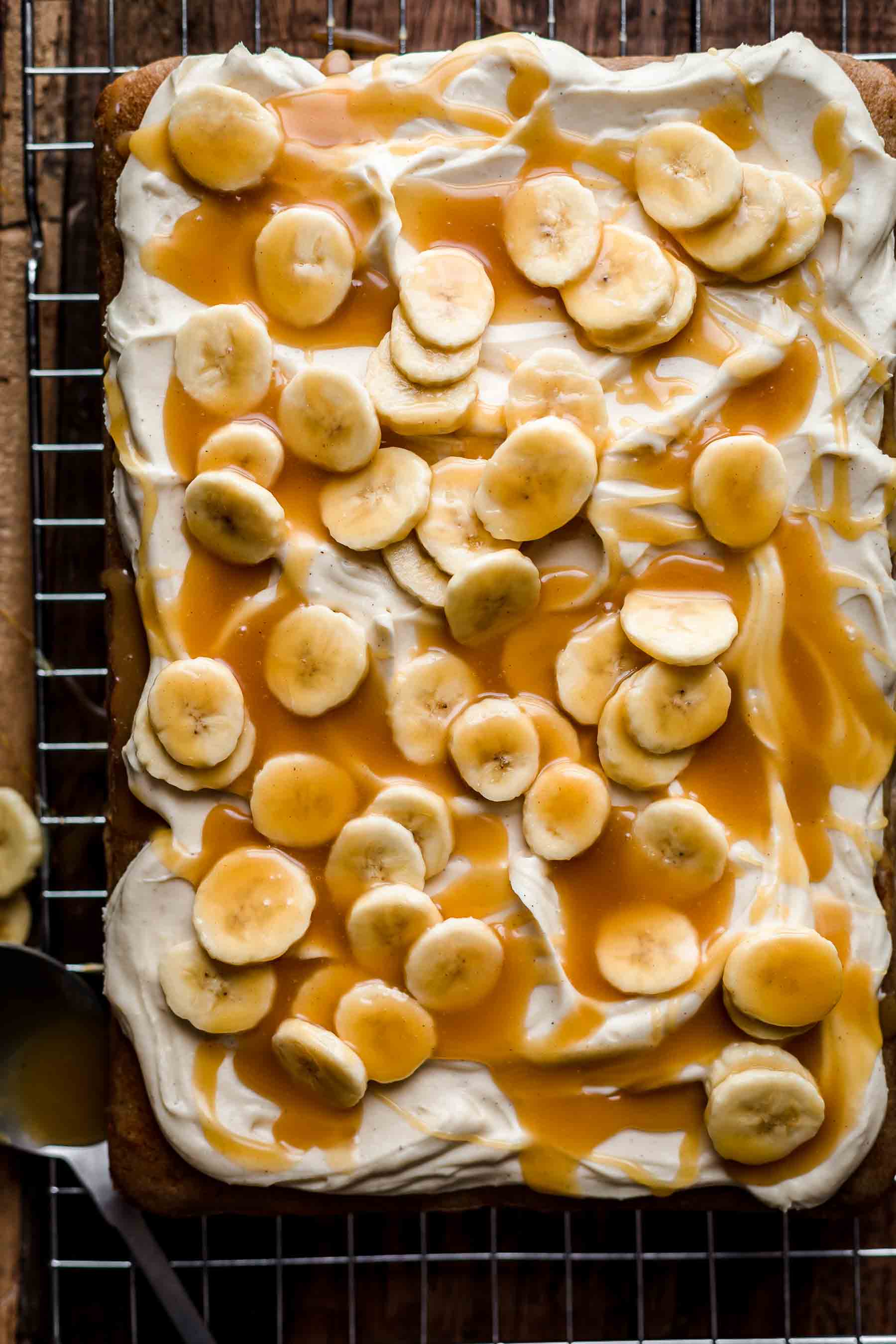 Baked Banoffee Cake on a cooling rack with fresh banana slices and caramel sauce on top